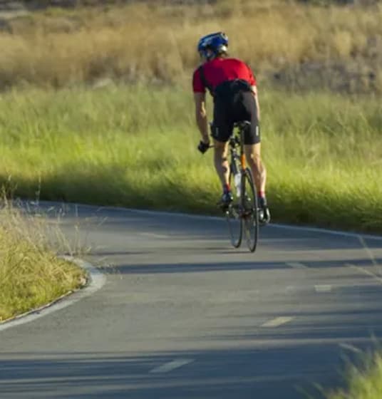 A cyclist rides on an open road through fields of grass